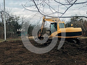 Excavator uprooting trees on land in countryside. Bulldozer clearing land from old trees, roots and branches with dirt and trash.