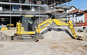 Excavator at work in front of residential building under construction.