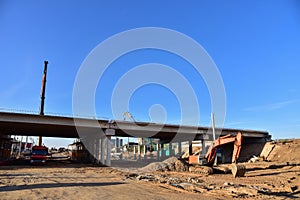 Excavator working at construction highway ramps and bridgeworks. Roundabout and traffic bridge construction. Road work on traffic