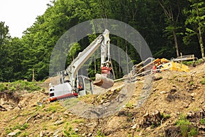 Excavator working on construction of higway on the steep slope of the hill.