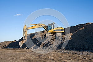 Excavator working at construction site. Backhoe digs ground in sand quarry on blue sky background. Construction machinery for