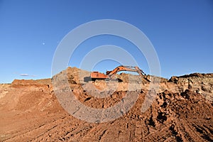 Excavator working at construction site. Backhoe digs ground in sand quarry on blue sky background. Construction machinery for