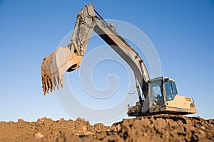 Excavator working at construction site. Backhoe digs ground in sand quarry on blue sky background. Construction machinery
