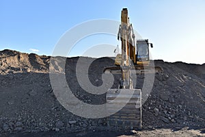 Excavator working at construction site. Backhoe digs ground in sand quarry on blue sky background. Construction machinery for