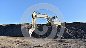 Excavator working at construction site. Backhoe digs ground in sand quarry on blue sky background. Construction machinery for