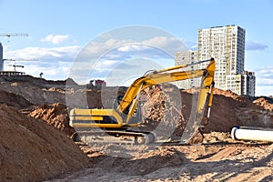 Excavator working at construction site on earthworks. Backhoe digs ground for laying concrete sewage pipes. Installing underground