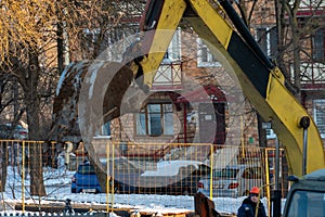 The excavator is working on the construction site to replace the pipeline in winter. Digging holes for laying new pipes for