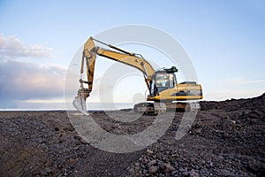Excavator working at open pit mining on sunset background. Backhoe digs gravel in sand quarry on blue sky background