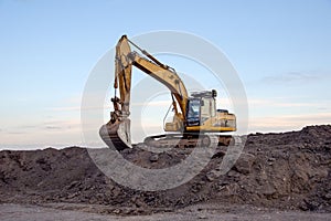 Excavator working at open pit mining on sunset background. Backhoe digs gravel in sand quarry on blue sky background. Recycling