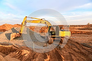 Excavator working on road work at a construction site on sunset background. Screeding gravel and ground for laying asphalt on the
