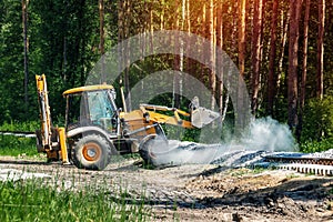 Excavator works on the construction of the railway in the forest. Yellow excavator pours the gravel between the sleepers
