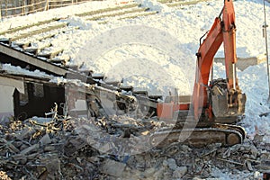 An excavator works at a construction site loading construction debris on a background of snow in winter in Russia