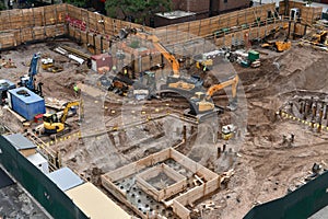 Excavators digging on skyscraper construction site with foundation pit.