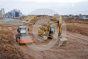 Excavators and soil compactor during road works at construction site. Backhoe digging the ground for the foundation and for laying
