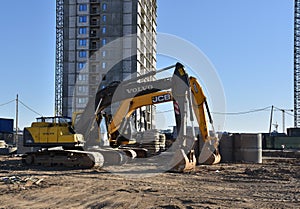 Excavators VOLVO and JCB on earthworks at construction site. Backhoe on foundation work and road construction. Tower cranes in