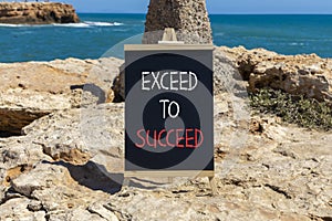 Exceed to succeed symbol. Concept words Exceed to succeed on beautiful black chalk blackboard. Beautiful red stone blue sea sky