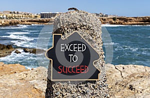 Exceed to succeed symbol. Concept words Exceed to succeed on beautiful black chalk blackboard. Beautiful red stone blue sea sky