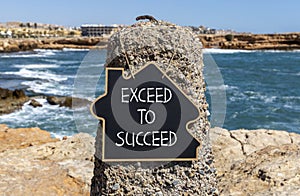 Exceed to succeed symbol. Concept words Exceed to succeed on beautiful black chalk blackboard. Beautiful red stone blue sea sky