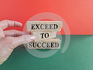 Exceed to succeed symbol. Concept words Exceed to succeed on beautiful brick blocks. Beautiful green table red background.
