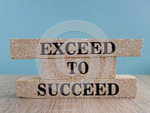 Exceed to succeed symbol. Concept words Exceed to succeed on beautiful brick blocks. Beautiful wooden table blue background.