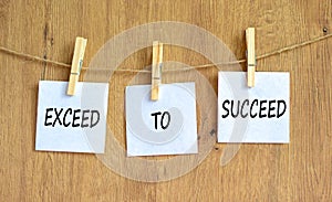 Exceed to succeed symbol. Concept words Exceed to succeed on beautiful white paper on clothespin. Beautiful wooden table wooden