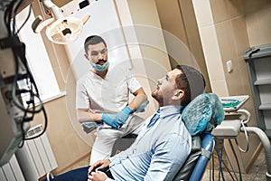 Excellence in dentistry with optimum care. Dentist in mask and latex gloves sitting near his patient in dental clinic