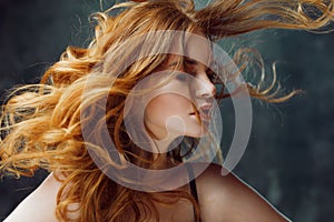 Excellent curly hair. Happy beautiful redheaded girl. Studio portrait on textured background. Flying long hair