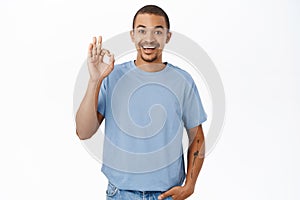 Excellent. Smiling arab man shows okay, ok sign in approval, agree with you, recommending, stands over white background