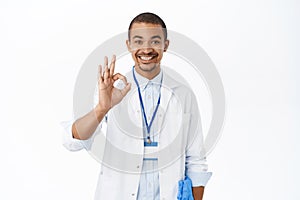 Excellent. Smiling doctor shows okay, ok sign, recommends smth to patient, assures everything good, stands over white