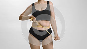 Excess weight caucasian woman with wrap measure tape around her waist. Still shot high quality video.