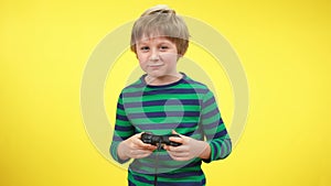 Excited absorbed kid playing game console and making victory gesture at yellow background. Portrait of happy carefree