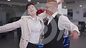 Excited adult couple rejoicing car winning in dealership in slow motion. Portrait of happy cheerful Caucasian husband