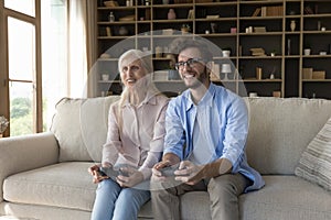 Excited adult grandson and cheerful grandma playing family video game