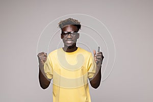 Excited african American male in glasses isolated on grey studio background hold smartphone happy wining online
