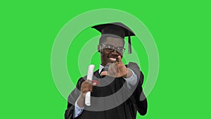 Excited african american male student in graduation robe waiving his diploma and posing for camera on a Green Screen