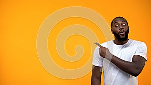 Excited African-American man pointing finger into background, template for text