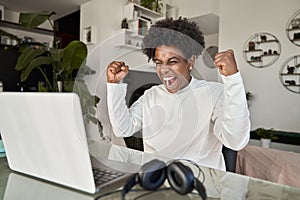 Excited African American student celebrating online win looking at laptop.