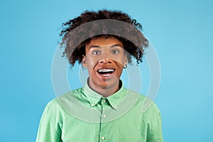 Excited african american teen guy with braces looking and smiling at camera, posing over blue studio background