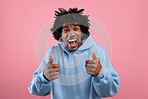 Excited African American teenager gesturing thumbs up with both hands, recommending something on pink background