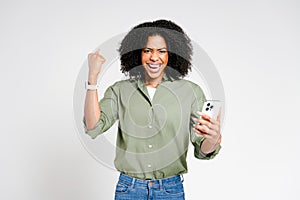 An excited African-American woman with a toothy smile celebrates a victory on her smartphone