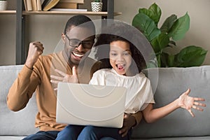 Excited african father and kid girl winners looking at laptop