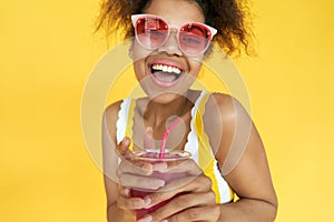 Excited african girl wear sunglasses hold drink look at camera in yellow studio.