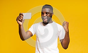 Excited African Guy Celebrating Success, Using Smartphone over Yellow Background