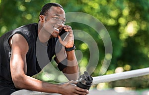 Excited african guy talking on phone during break, exercising outdoors