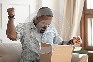 Excited african man customer receive open parcel box at home