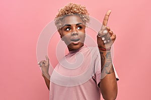 Excited African woman index finger showing something surprising on pink wall