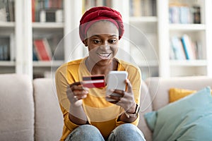 Excited african woman using cell phone and bank card