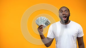 Excited Afro-American man holding bunch of dollar, crowd funding or start-up