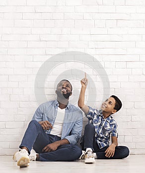 Excited Afro Boy Sitting On Floor With Father And Pointing Upwards