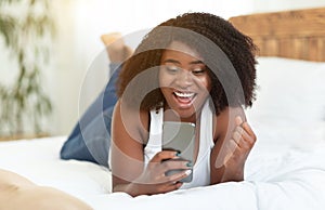 Excited afro girl feeling ecstatic holding phone